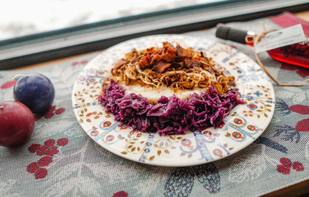 A platter of mashed potatoes, fried onions, and bacon, surrounded by red cabbage salad.